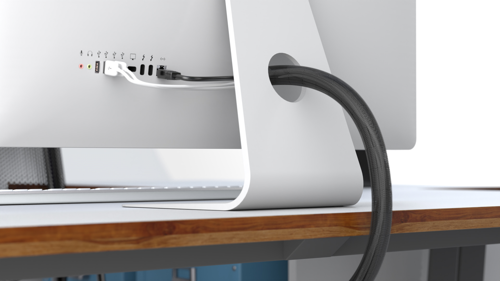 Ein iMac Rechner mit zwei USB Kaeln und einem LAN Kabel. Die kabel sind mit einem kabelschlauch zusammengehalten. Das Gerät steht auf einem Schreibtisch mit Holz-Optik. Daneben ist eine tastatur und ein Büro-Stuhl zu sehen. Das Bild wurde mit Cinema 4D und ProRender gerendert und war teil eines Kundenauftrags zur 3D-Visualisierung von Lösungen für Kabelsortierungen.